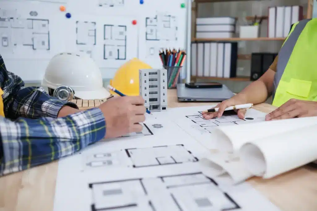 Équipe d’architectes examinant des plans de construction dans un bureau, avec maquettes et équipements techniques.